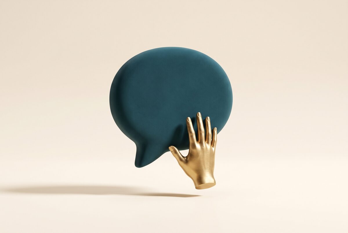 A matte teal speech bubble held back by a brushed-gold hand: a message paused before it lands.